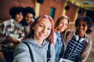 Happy teenage girl and her friends taking selfie at high school.